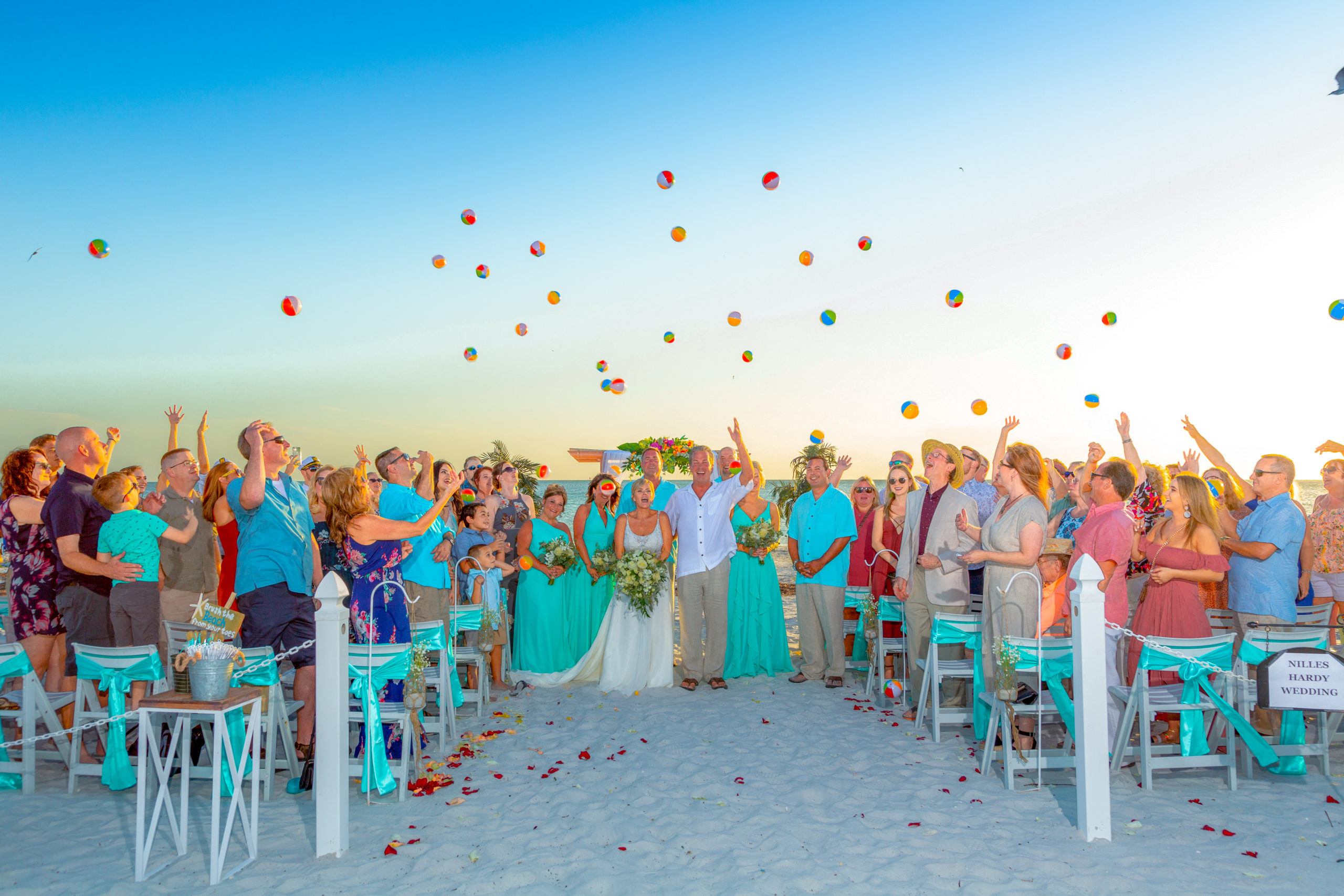 A group of wedding guest throw beach balls into the air.